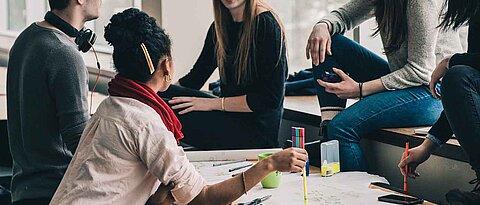 Man sieht eine Gruppe von Studierenden, die im Kreis sitzen und sich unterhalten.